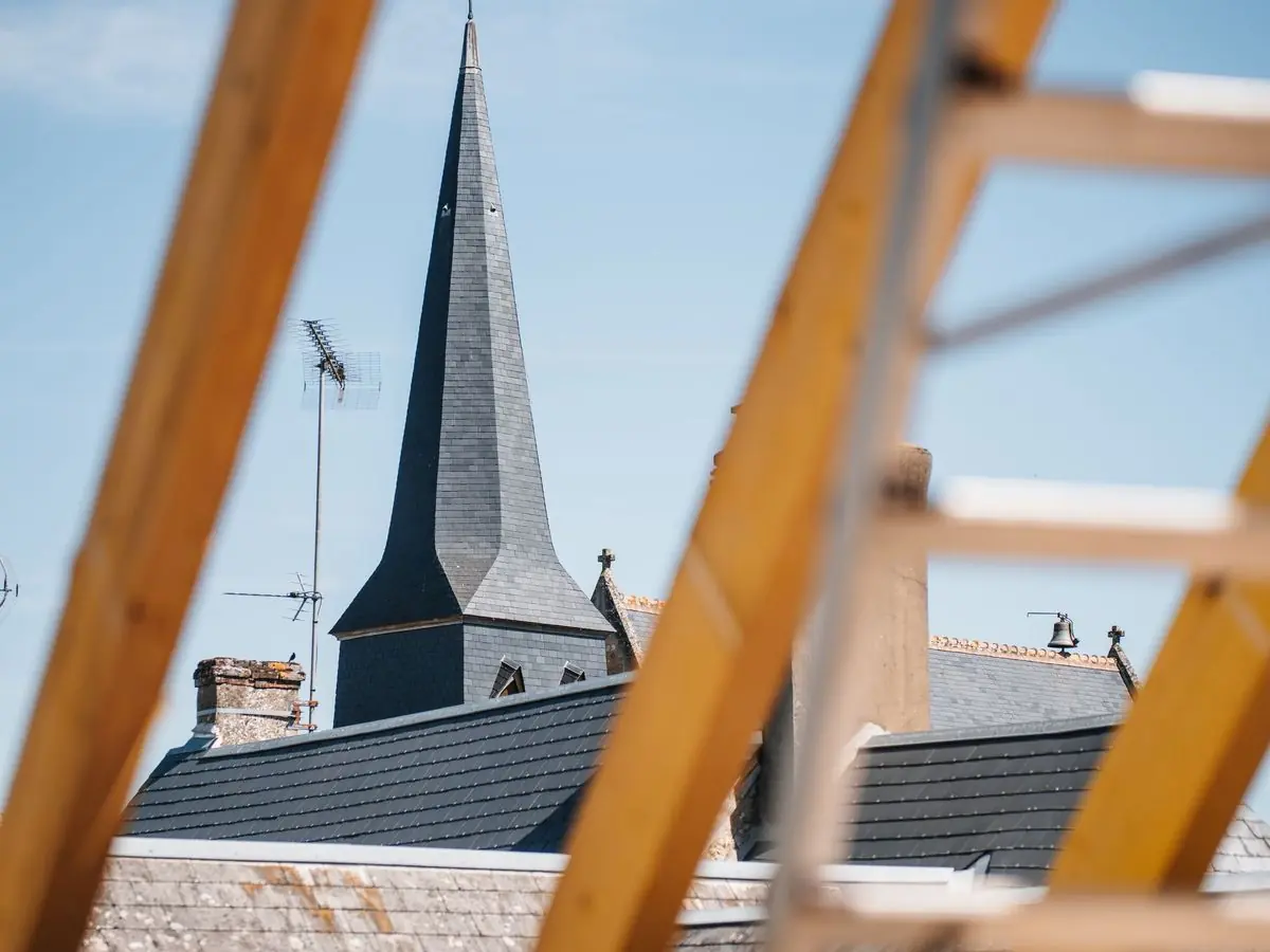 Un artisan au travail sur une toiture près d'un clocher